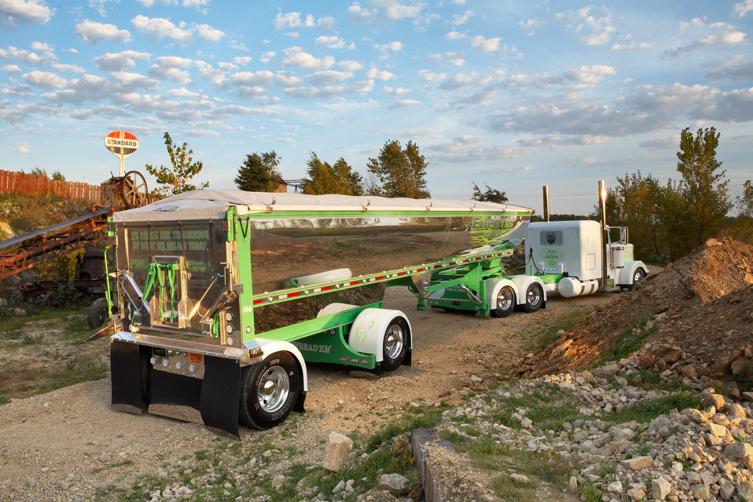 A fancy Peterbilt Model 379 and shiny Mac end-dump trailer bask in evening light.