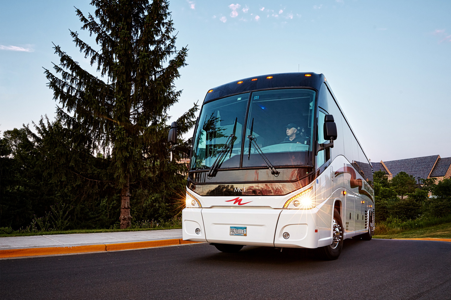 An MCI motor coach rounds a corner on a college campus in Minnesota.