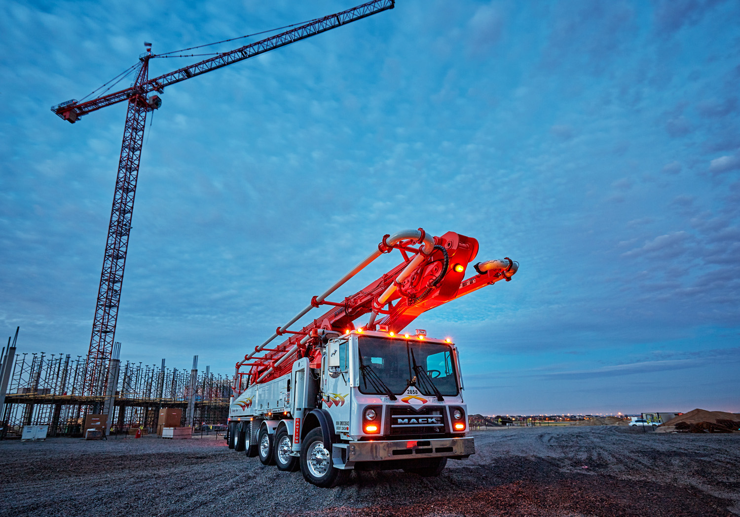 A six-axle Mack truck fitted with a concrete pumper waits at a job site.