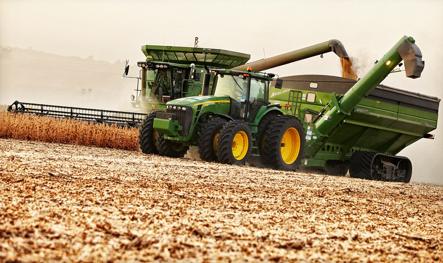 A John Deere combine unloads soybeans into a nearby gravity box without stopping